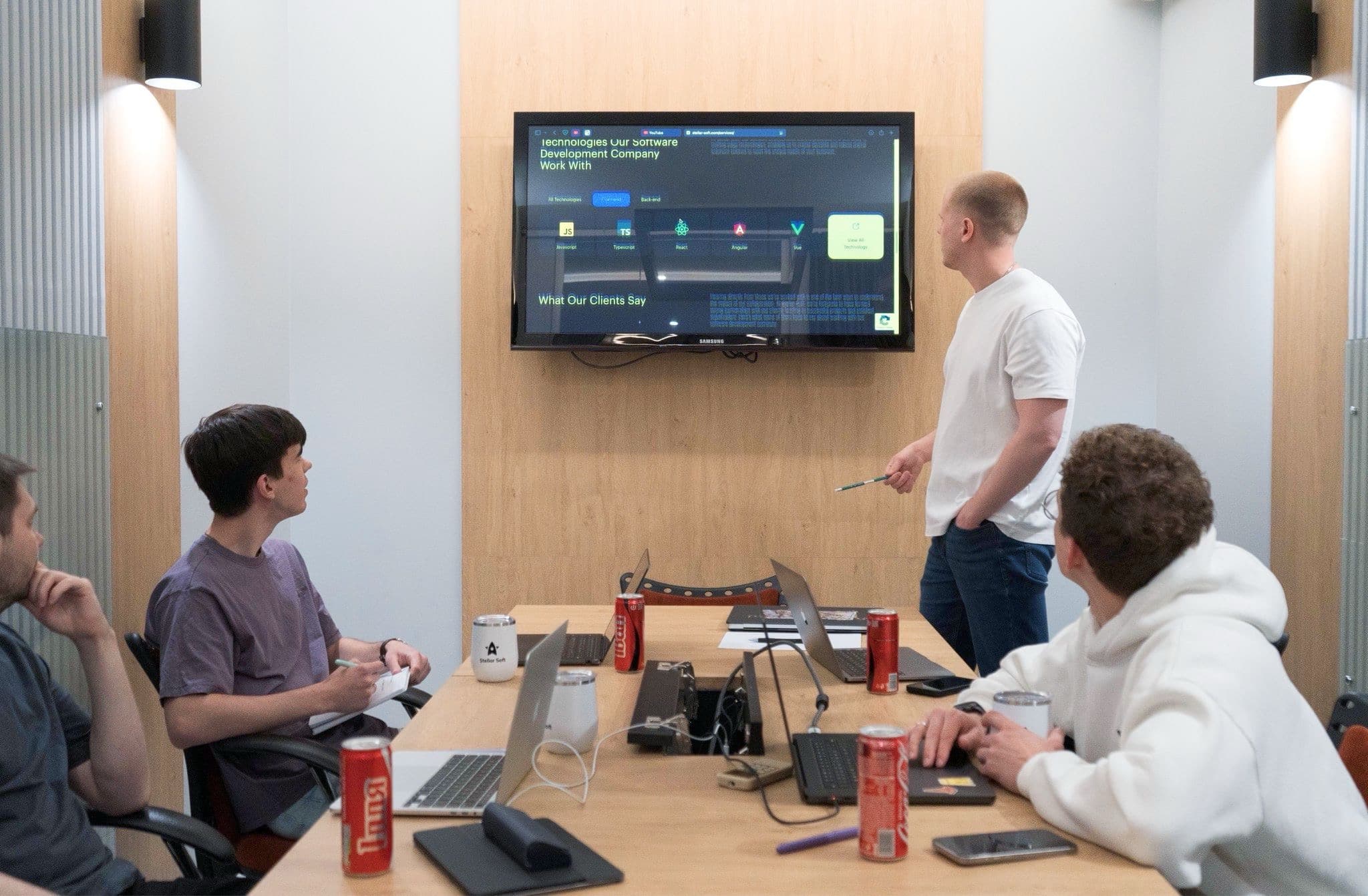 Team brainstorming in conference room with screens, laptops, and drinks.