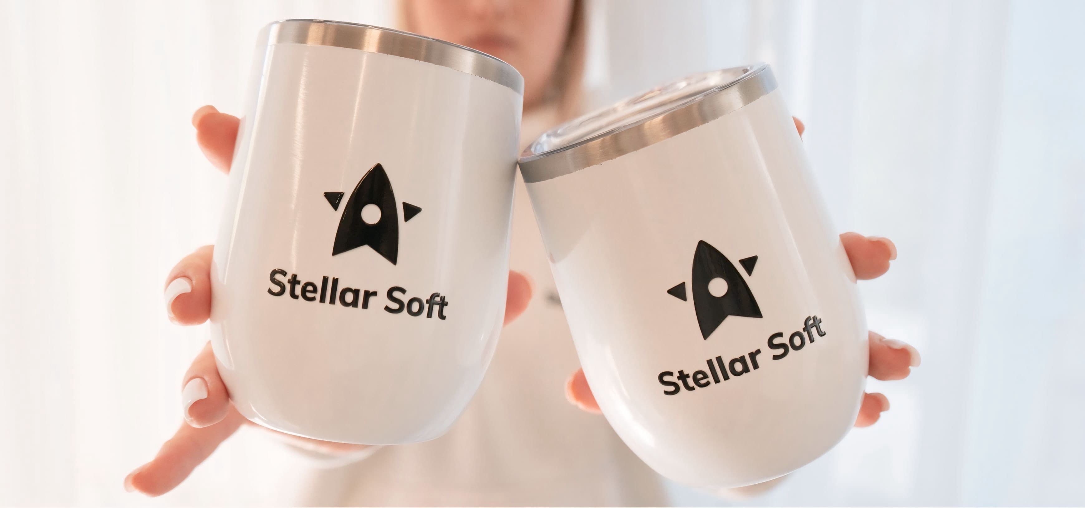 Two insulated mugs with "Stellar Soft" logo, held by a person.