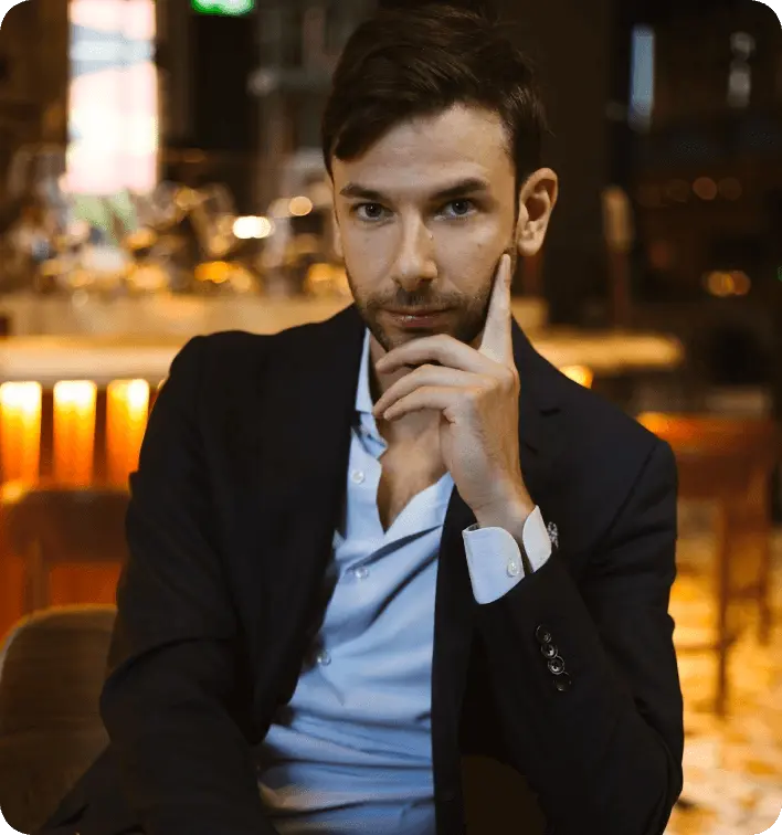 Man in a suit sitting thoughtfully in a warmly lit bar.